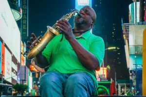 A street musician in a green shirt plays the saxophone in the vibrant setting of Times Square. #About BaoLiba – Transforming Influencer Marketing in the USA