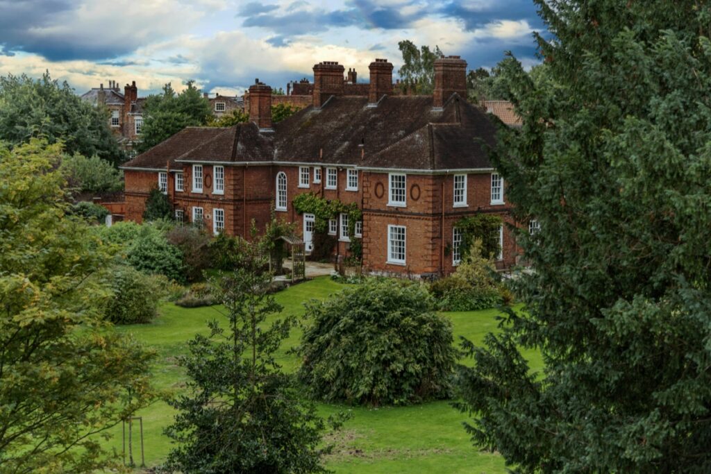 This image depicts a charming red - brick house surrounded by lush greenery, including well - maintained lawns and a variety of trees. The house features multiple chimneys and white - framed windows, giving it a classic and inviting look. In the context of "How to Use Hashtags on Twitter to Improve Brand Engagement in the USA", brands can use relevant hashtags when sharing images like this. For example, if the brand is related to home decor, real estate, or gardening, hashtags such as #HomeSweetHome, #RealEstateUSA, or #GardeningTips can be used. This helps the content reach a wider audience interested in these areas, thereby enhancing brand engagement on Twitter.